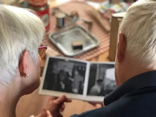 Två äldre personer ses bakifrån. De tittar i ett fotoalbum med svartvita bilder i.