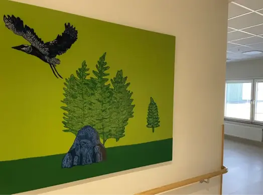 Textilt verk med två gröna fält i bakgrunden. Till vänster syns en större svart fågel som flyger iväg, i mitten stora gröna blad och en sten. 